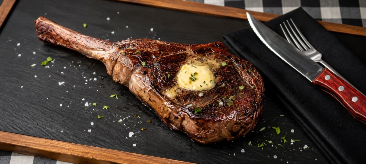 Grilled tomahawk bison ribeye steak on a slate board.