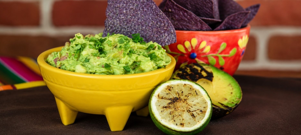 Grilled guacamole, tortilla chips, a grilled lime half and grilled avocado half.