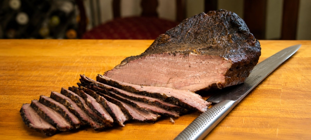 Sliced sous vide and smoked brisket and a knife on wood cutting board