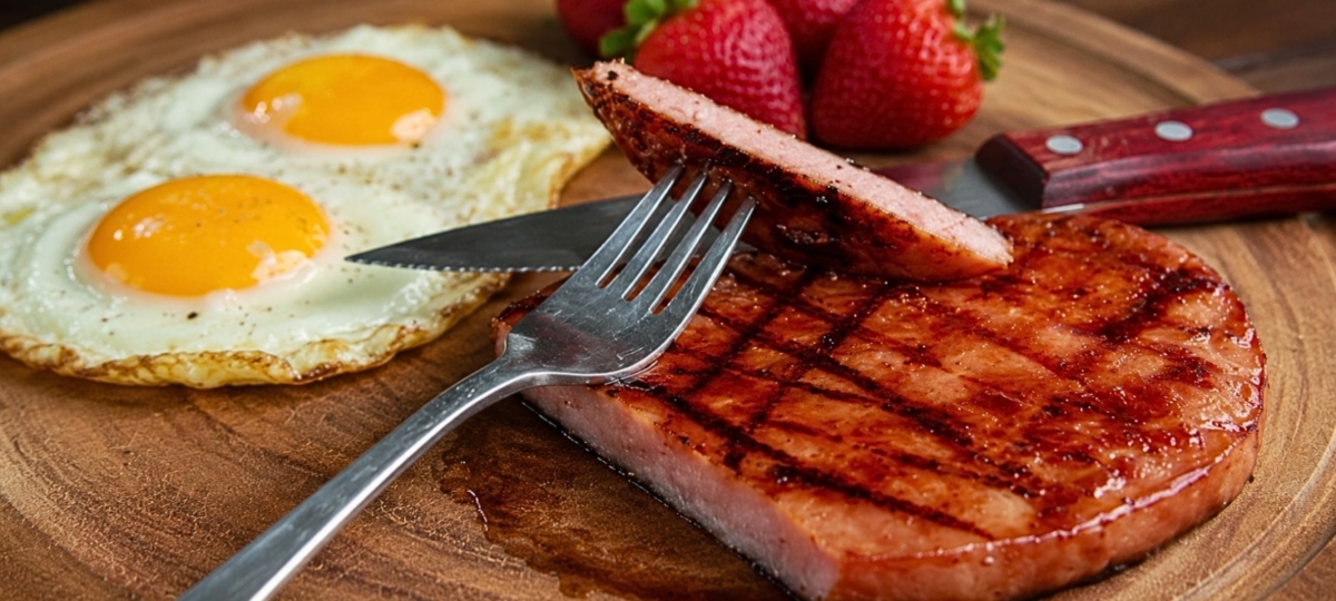 Grilled glazed ham steak plated with eggs and fruit.