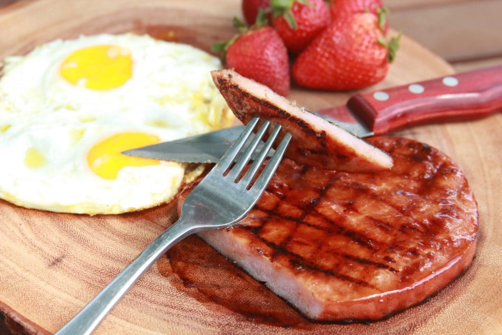 Grilled glazed ham steak plated with eggs and fruit