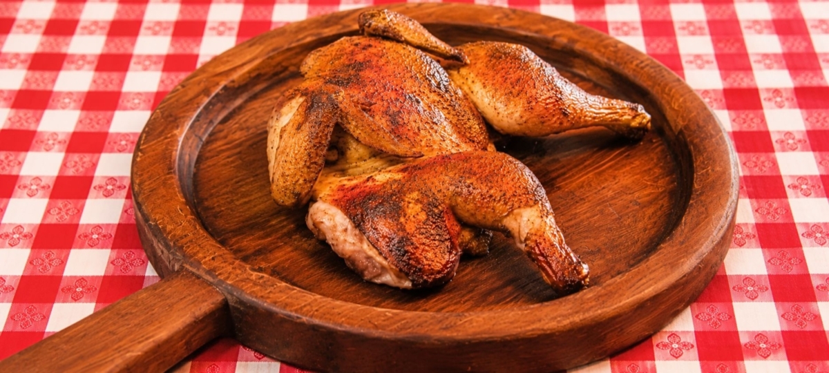 Spatchcocked chicken on wooden board and checkered tablecloth.