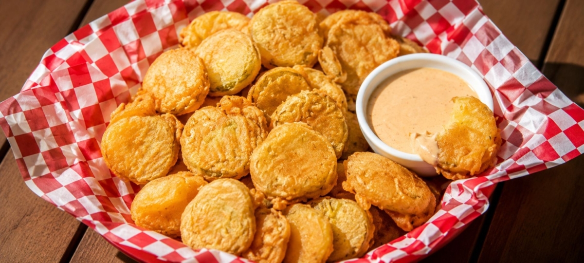 Deep fried pickles in a serving platter lined with red checked paper.