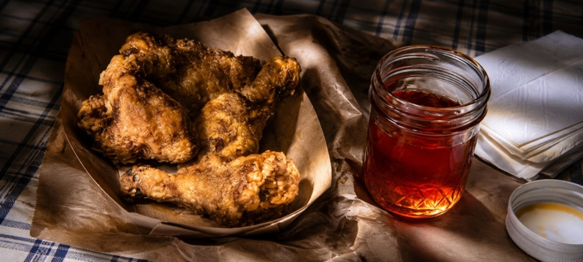 Nashville hot chicken in serving basket alongside a jar with sauce.