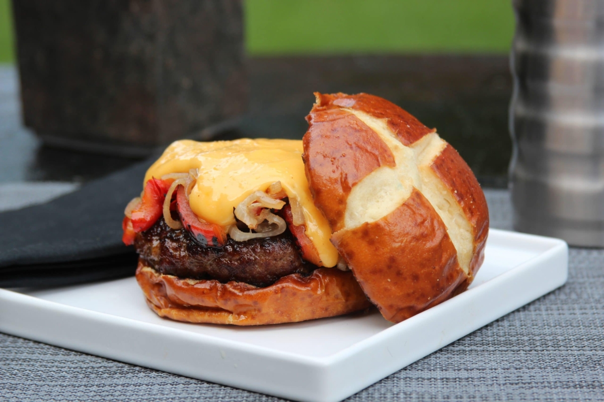 Brat burger with cheese sauce on a pretzel bun