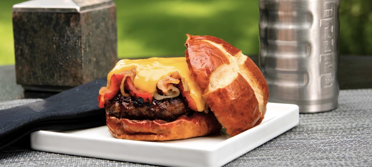PLated brat burger with cheese sauce on a pretzel bun