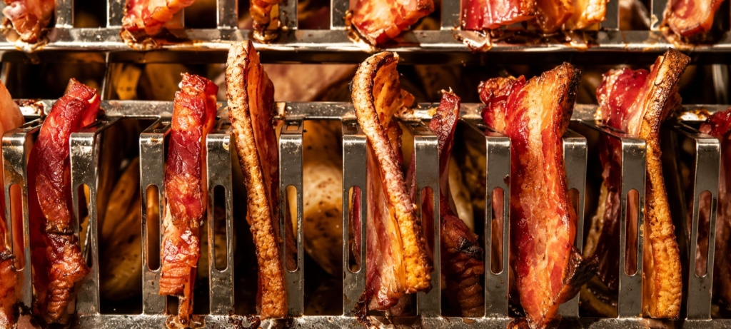 Pork belly slices hanging from rods.