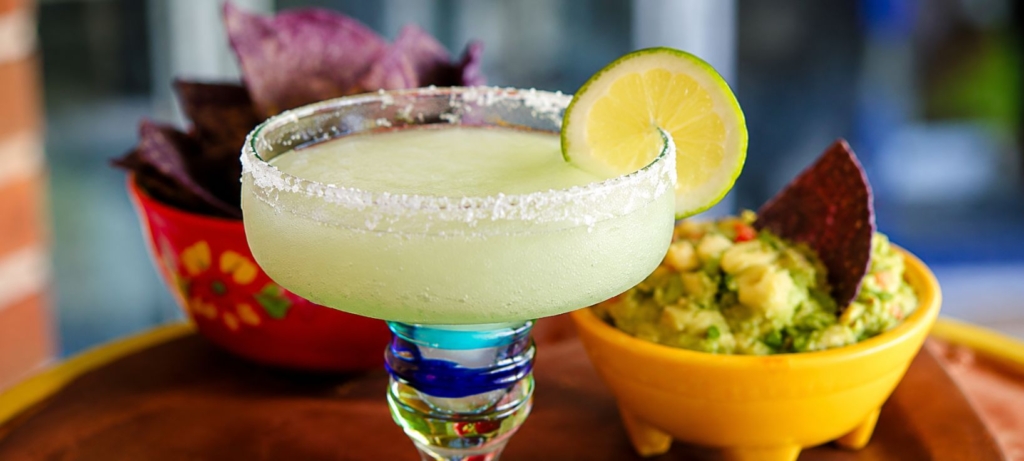 Grilled lime margarita in salt rimmed glass with chips and guacamole in the background.
