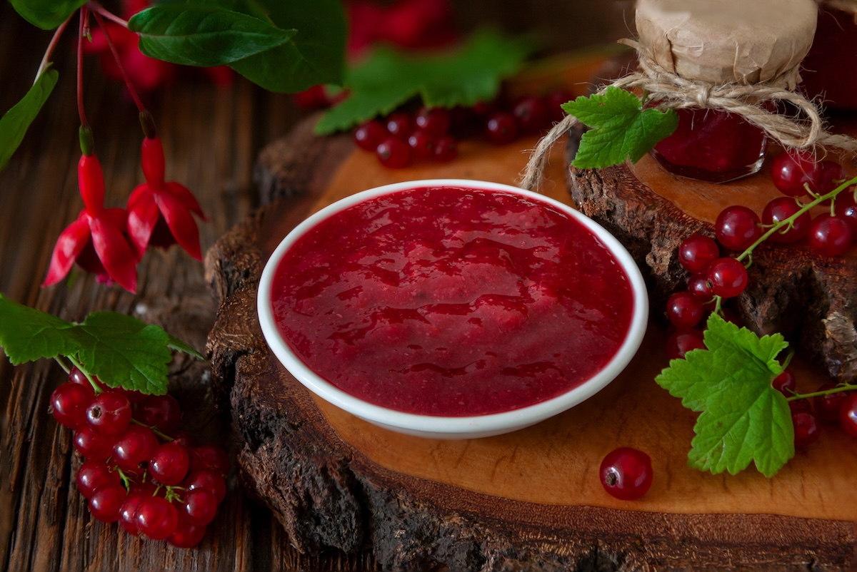 homemade cumberland sauce in a white bowl on a wooden table with fresh red currants