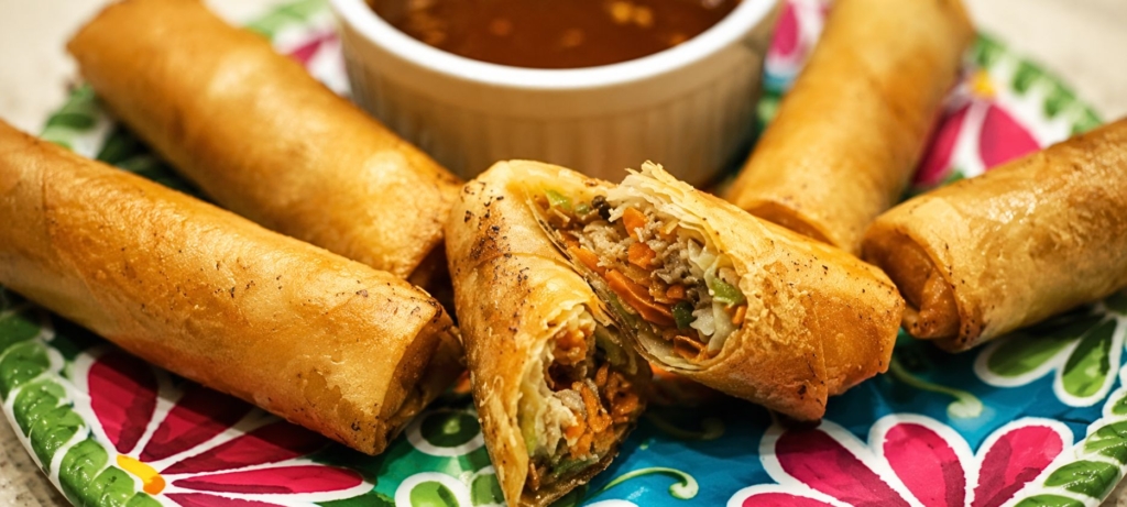 Pulled pork egg rolls on a colorful plate with a small bowl of dipping sauce.