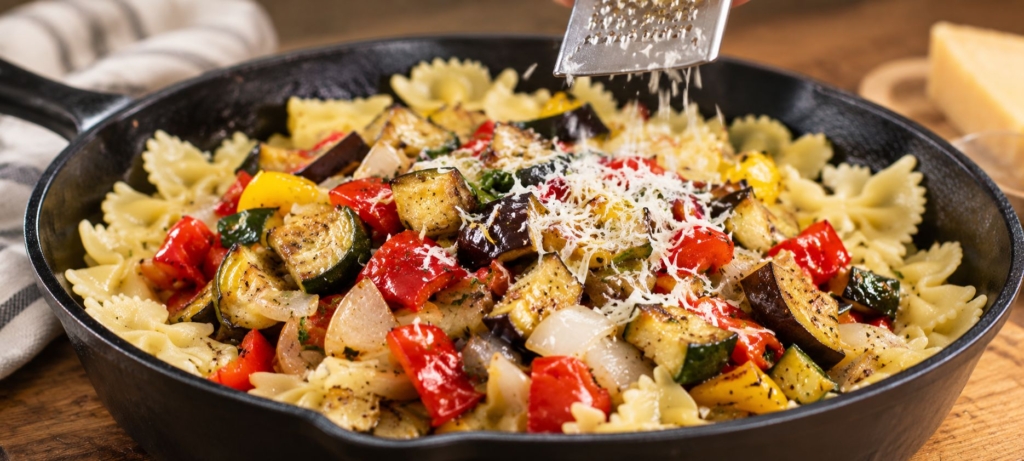 Grilled ratatouille in a cast iron skillet with cheese being grated over the top.