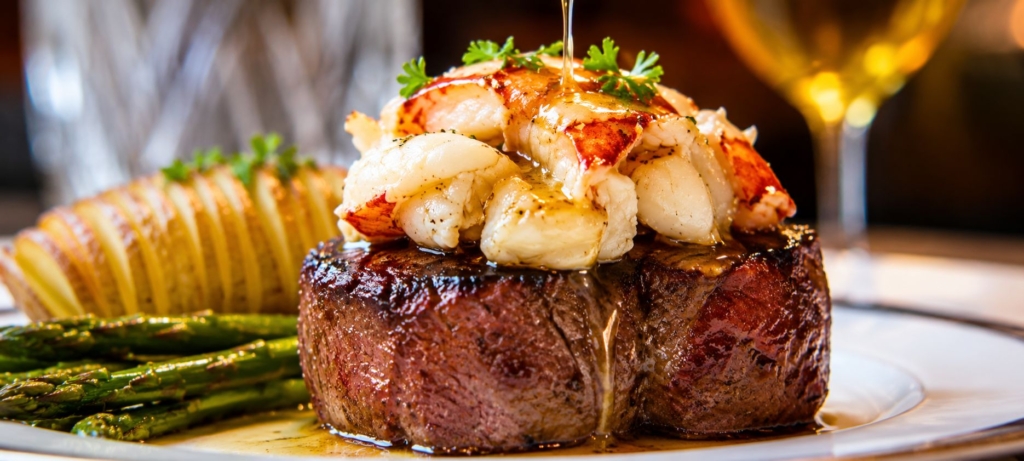 Plated smoked filet mignon topped with lobster and drizzled with butter and accompanied by a hasselback pottato and asparagus.