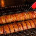 bacon wrapped venison backstrap on grill and a red thermometer