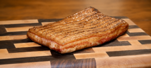 Unsliced maple bacon on a wooden cutting board.