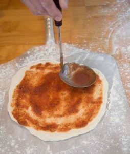 adding pizza sauce