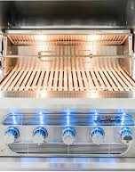 stainless steel gas grill with blue LED lights on each dial and bright halogen lights in the hood
