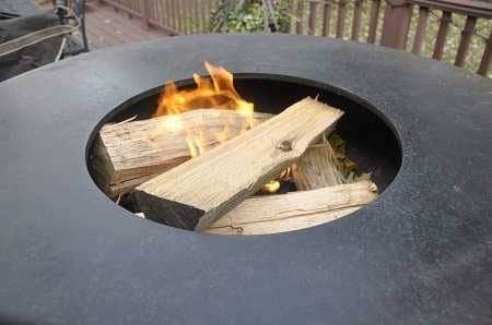 Round metal bowl filled with burning wood on an outdoor deck.