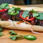 Baguette, split and filled with meat, red and green jalapenos, and garnished with cilantro