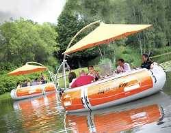 Two round orange and white boats with large orange umbrellas floating down a river in a forested area.