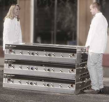 A woman and man in white catering outfits stand on each side of a stack of large gas grills. The gas grill legs are folded up to allow stacking.