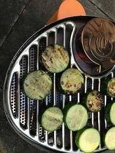 Oval shaped shiny steel grill grate cooking round slices of zucchinis.