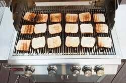 18 slices of toastedbread spread over the cooking surface of a gas grill, Some pieces are a little more toasted than others. pie