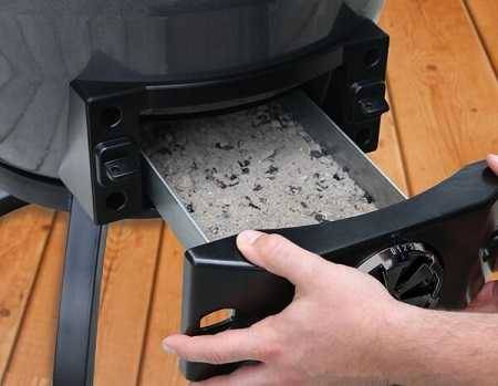 hands pulling our a tray filled with ashes at the bottom of a kamado smoker.