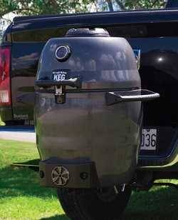 Steel kamado charcoal cooker mounted to the back of a truck on a trailer hitch.