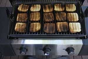 gas grill from above with the lid up to show  toasted bread covering the cooking surface.