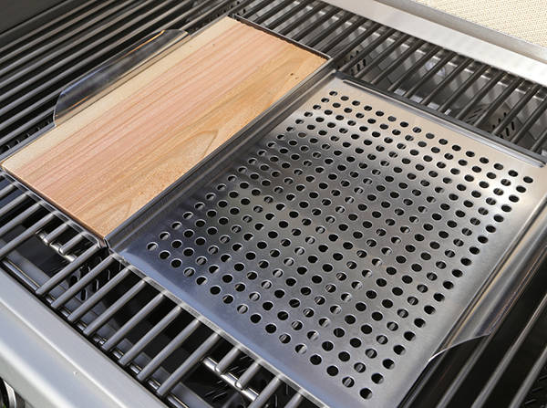 Shiny stainless steel gas grill with lid up showing a a wood plank an perforated metal tray set on the cooking grates.