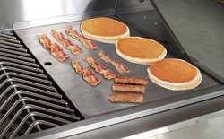 Flat griddle cook surface on a stainless steel gas grill cooking grate, cooking bacon and eggs.
