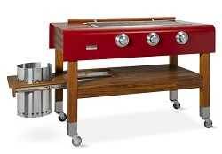 A red gas grill with no lid mounted on a beautiful wood frame with four legs and four wheels. A large steel can is sticking out on the left.