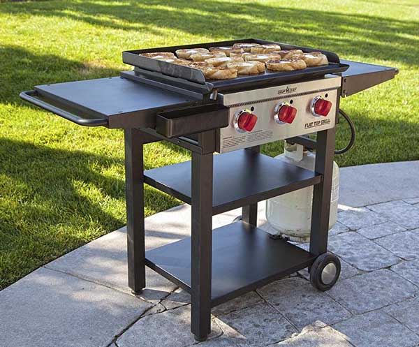 Outdoor griddle on four legged cart placed on a brick walk way. Three red dials are on the front.
