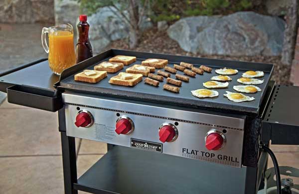 Large outdoor griddle loaded with toast, sausage and eggs. Four red dials are on the front.