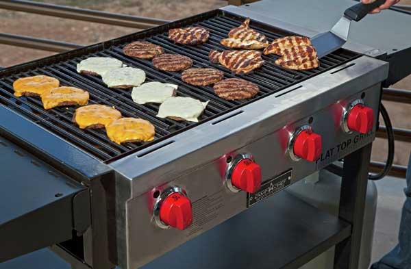 Large outdoor gas grill loaded with hamburgers and grilled chicken. Four red dials are on the front.