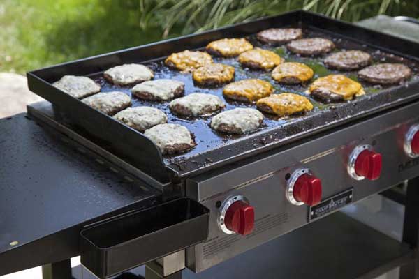 Large outdoor gas grill loaded with hamburgers and grilled chicken. Red dials are on the front.