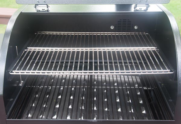 Black cooking grates with a shiny metal plate underneath. Shiny metal cooking grates are slid into a rack above the black grates.