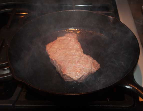 Pale grayish steak in a sizzling cast iron skillet