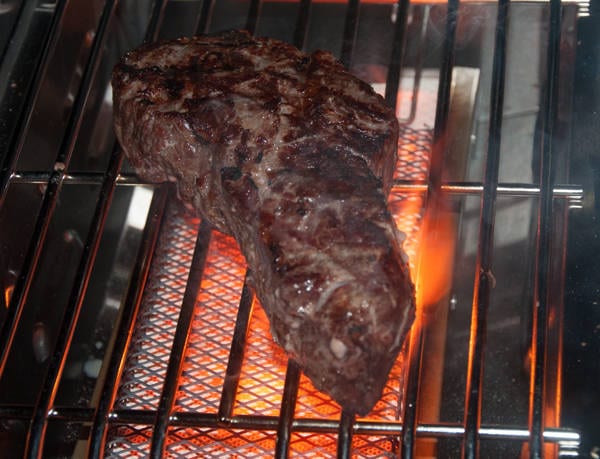 Steak getting searing over a hot, flaming burner.