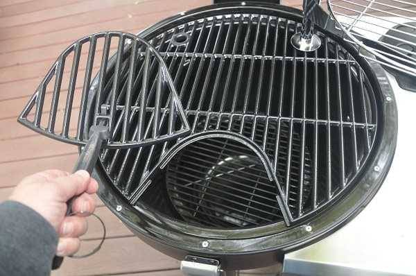 A deep black bowl on an outdoor deck with a black grate on top. A hand on the left is holding a half-moon shaped piece of the grate that has been removed.