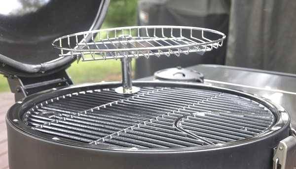 A round black grate on a round object placed on an outdoor deck. A smallet, shiny metal round grate is stuck into the black grate with a small pipe.