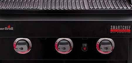 Front of a black gas grill. There are three gas burner control knobs with red lights.