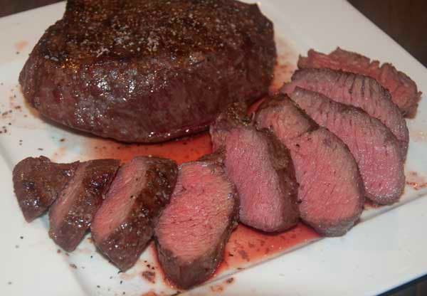 steak on a white plate. some steak is sliced showing juicy, pick interior