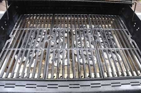 A bbq grill from above with lid up showing the cooking grates. Beneath the grates is a bed of hot charcoal.