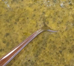 A spoon dips into a pale green spread