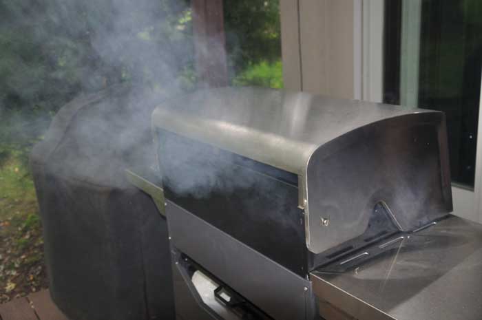 Smoke billowing out the back of a gas grill.