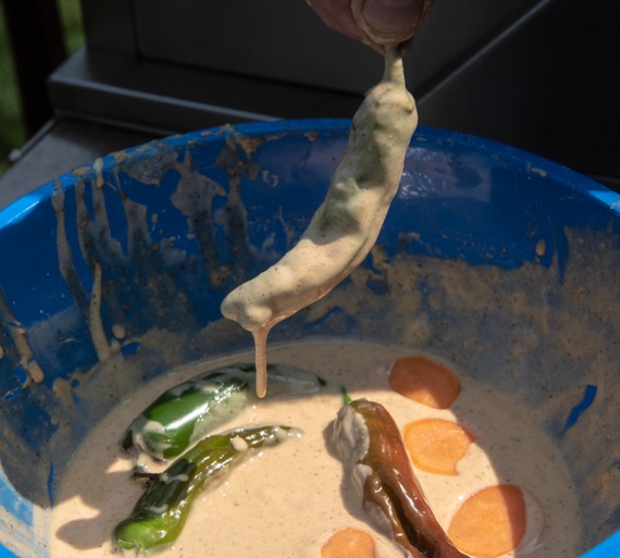 Dunking a chile pepper into a wet batter.