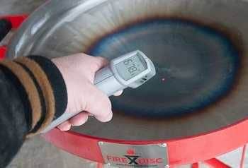 Metal disc with hot spot in the middle. A hand holds an infrared thermometer which show the disc center is 678 degrees Fahrenheit.