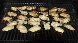 A bbq grill cook surface from above loaded with chicken wings. The wings in the are cooking faster than those up front which are still raw.