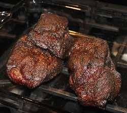 Two brown smokey hunks of meat on a bbq grill grate.